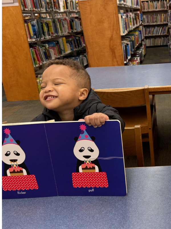 A smiling toddler holding up a panda picture book
